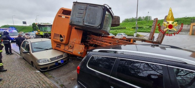 Escavatore scivola dal rimorchio e va a sbattere contro auto in sosta
